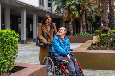 Smiling caregiver pushing wheelchair, sharing warm conversation and laughter with happy man