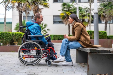 Man with a disability in a wheelchair having a cheerful conversation with a woman sitting on a park