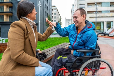Young man with a disability sitting in a wheelchair and joyfully high fiving a woman sitting on a