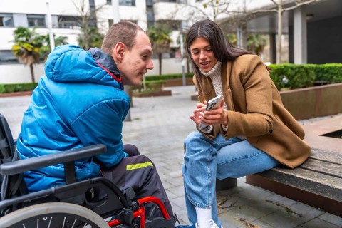 Young woman sitting on a bench, showing content on a smartphone and engaging in communication with