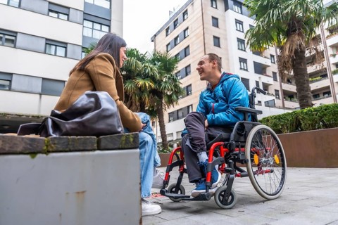 Young man with disability in a wheelchair discussing and smiling with a caring woman sitting on a