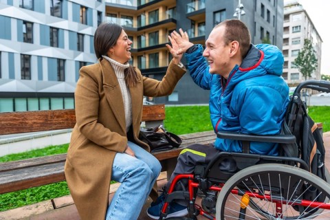Woman and disabled man in wheelchair laughing, high fiving, and sharing a happy moment during an