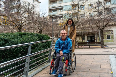 Happy woman caregiver assisting a young man with a disability, pushing him in his wheelchair along