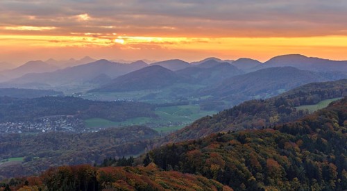 View of an autumnal forest from the Gisliflue, behind the Jurassic foothills in the light of the