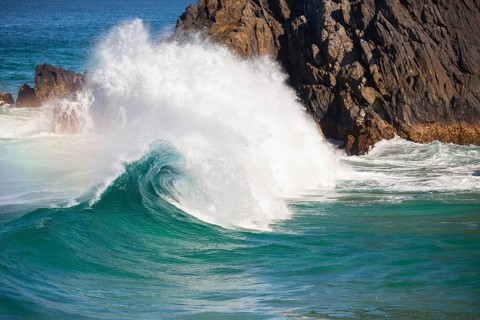 Waves crash against rocks at the mainland's easternmost point, creating rainbows in the ocean spray