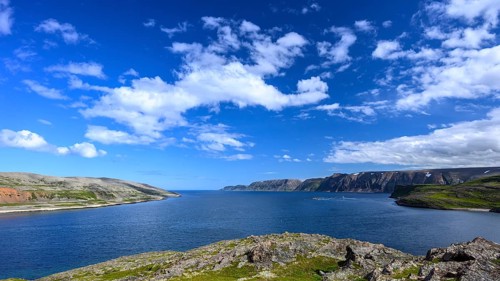 Green meadows on the banks of Syltefjord with clouds in the blue sky, landscape with a lake and
