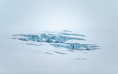 Smooth white snowy area on the glacier broken by crevasses with blue rugged glacial ice, detail,