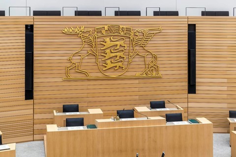 Plenary hall deserted with the seats of deputies and the government bank. Behind it is the coat of
