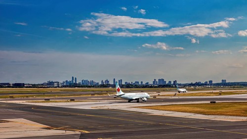 Airport with plane taking off in front of a skyline under a partly cloudy blue sky, view from an