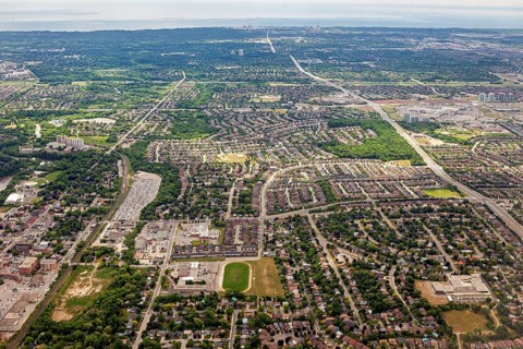 Densely populated residential areas and green spaces stretch out under a cloudy sky seen from the