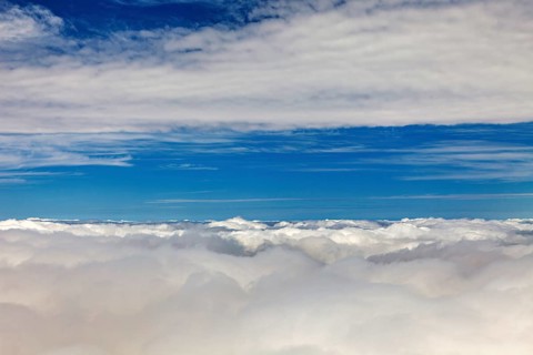 Wide view of white clouds under bright blue sky, on an airplane above the clouds