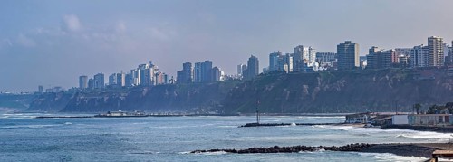 View of a coastal town with skyscrapers on cliffs and waves under a blue sky, The coast with the