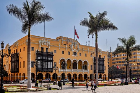 Colonial building with arches and national flag, surrounded by palm trees, in a sunny square, The