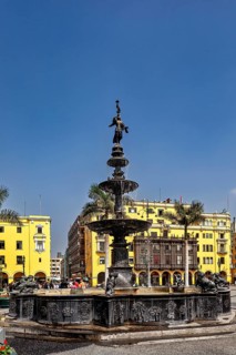 Historic fountain in a square with yellow buildings and palm trees under a blue sky, The historic