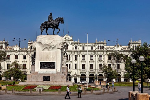 Equestrian statue on a large pedestal in front of an imposing historic building under a blue sky,