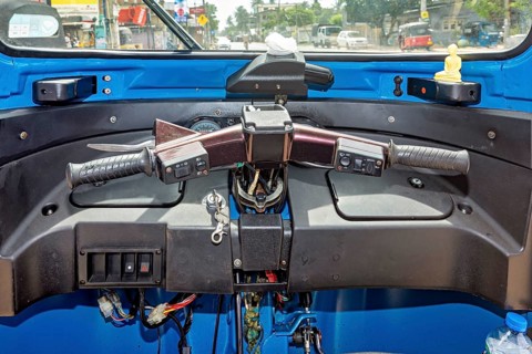 The picture shows the cockpit of a blue car rickshaw in an urban environment, the cockpit of a tuk