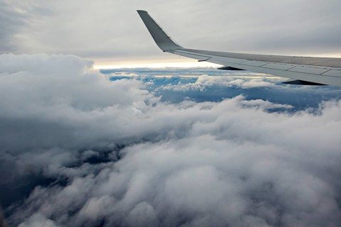 View of airplane wings above a thick cloud cover in the sky, In an airplane above the clouds