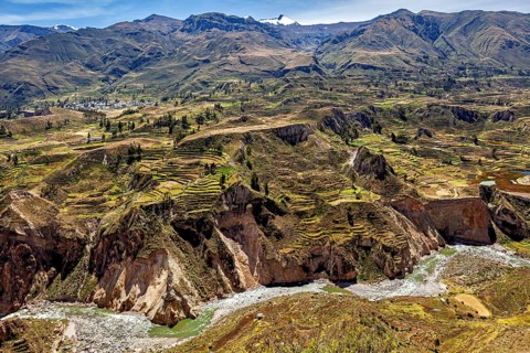 Mountain landscape with terraced fields and a river surrounded by green nature under blue skies,