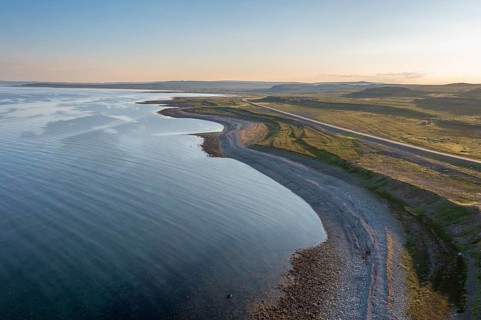 Coastal landscape on Varangerfjord with blue sky, still sea, moors and pebble beach aerial view,