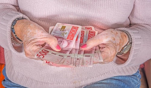An elderly woman's hands holding Swedish 500-krona banknotes