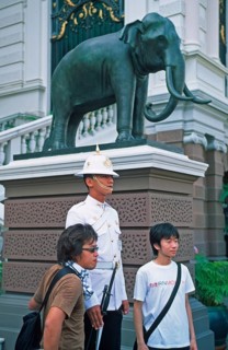Tourists pose for photo in front of palace guard, Grand Palace at Wat Phra Kaeo, Bangkok, Thailand,