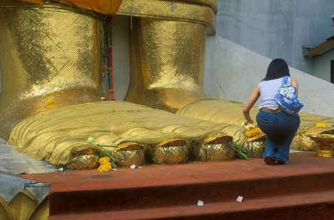 A young woman places flowers on the toes of the standing Buddha at Wat Indrawihan, Bangkok,
