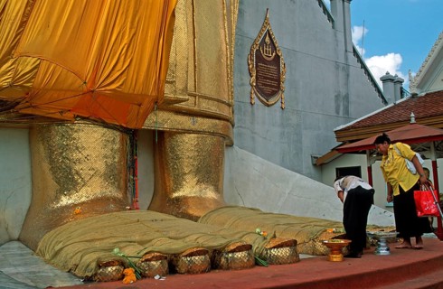 Women place flowers on standing Buddha's toes at Wat Indrawihan, Bangkok, Thailand, December 2002,