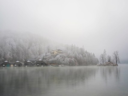 View across Königssee to boathouses, Christlieger island and frozen trees in fog, Schönau am