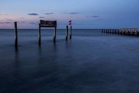 Wooden sign in the sea with inscription Zingst and wooden walkway, long exposure, evening light,