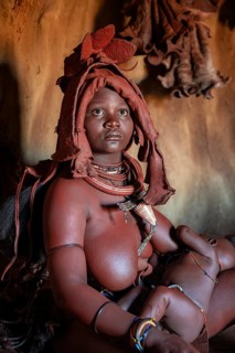 Himba woman sitting with baby in traditional hut, Himba village, Kaokoveld, Kunene, Namibia