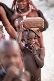 Himba woman and children run to fetch water with canisters through dry countryside, traditional