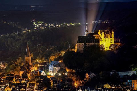 Castle and church shine in night lighting on a wooded hill. The Landgrave's Castle of Marburg in