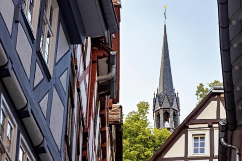 View of a narrow street with half-timbered houses and a church tower in the background, The