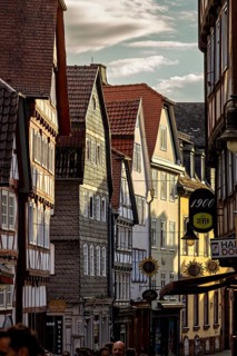 Narrowly built street with historic half-timbered houses and people passing by in the evening