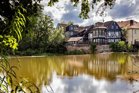 Half-timbered houses are reflected in the water in partly cloudy skies. The historic houses of
