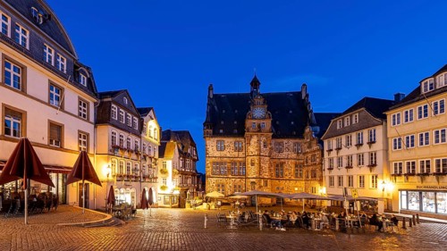 Historic square at dusk, surrounded by half-timbered houses and cobblestones, illuminated by warm