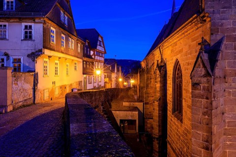 Historic street view at dusk with illuminated half-timbered houses and a church building, At the