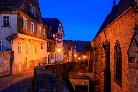 A nocturnal old town with half-timbered houses and cobblestones, warm lantern light creates a