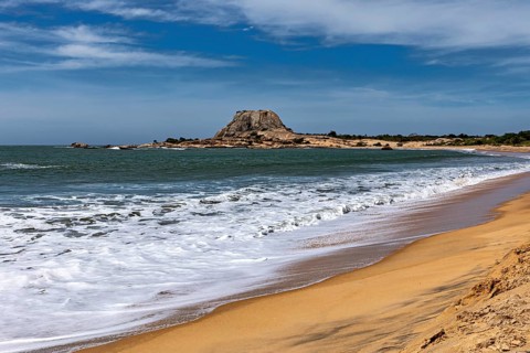 A peaceful coastal scene with sandy beach, turquoise ocean and distant rocks under blue skies, the