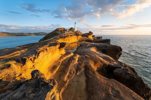 Castlepoint lighthouse on a rock, sea, sunrise. Castlepoint, Wairarapa Coast, Wellington Region,