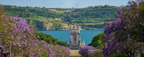 Scenic view of Belem Tower in Lisbon, Portugal, seen over a street with blooming purple jacaranda