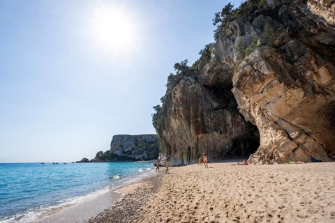 Sandy beach beach and steep cliffs with caves at Cala Luna, Golfo di Orosei, Baunei, Sardinia,