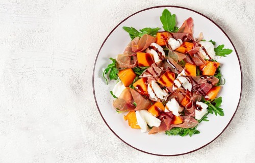 Salad with slices of ripe melon, prosciutto, mozzarella and fresh arugula, decorated with balsamic