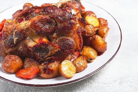 Pork knuckle baked with vegetables, new potatoes, on a white plate, homemade, no people