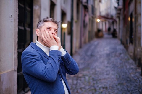 Man musician in a blue blazer and white sweater playing blues on a harmonica with eyes closed,