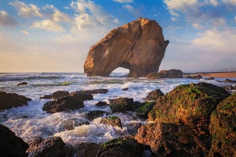Penedo do Guincho, a large boulder rock arch at Praia da Santa Cruz, Portugal, with ocean waves and