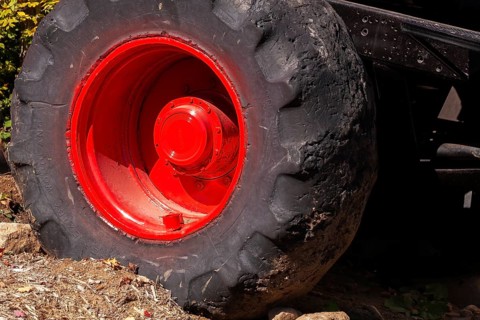 Close-up and rear side view of large heavy duty black rubber tire mounted on red rim on monster