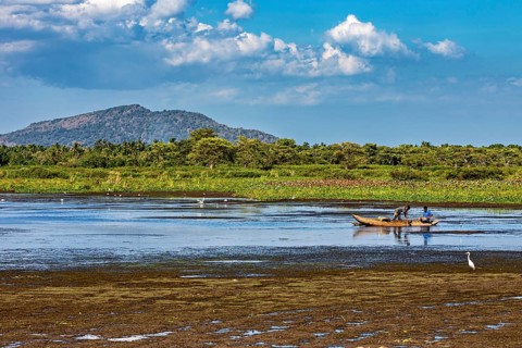 A small boat on a lake in a peaceful landscape with mountains in the background and a sky full of