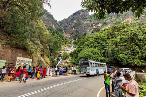 Mountain road with a bus and people looking at a waterfall surrounded by green mountain scenery,