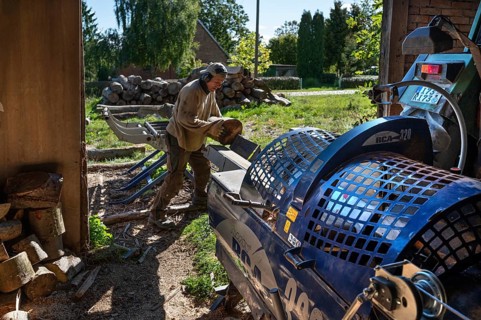 Young man sawing and splitting beech logs with his saw cutting machine, powered by a tractor in a